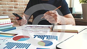 Businessman uses a smartphone, checking financial report and charts in the office at the workplace.