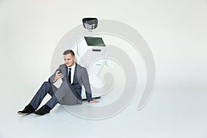 Businessman uses a smartphone while sitting on the floor next to a robot. Modern Robotic Technologies. Humanoid