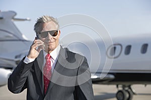 Businessman Using Cell Phone With Private Jet In Background