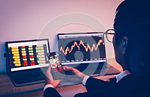 Businessman using cell phone with statistic graph of stock market analysis on laptop screen and technology.