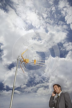 Businessman Using Cellphone Against Satellite Tower And Clouds