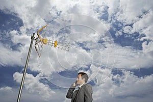 Businessman Using Cellphone Against Satellite Tower And Clouds