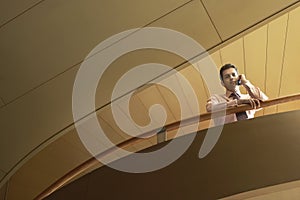 Businessman Using Cellphone While Leaning On Railing In Office