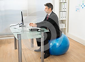 Businessman using computer while sitting on pilates ball