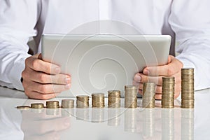 Businessman Using Digital Tablet With Stacked Coins At Desk