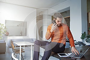 Businessman using his mobile phone and talking with somebody while sitting at office desk