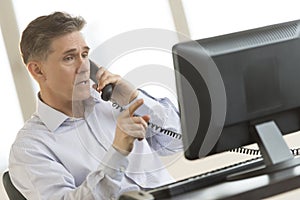 Businessman Using Landline Phone While Pointing At Computer