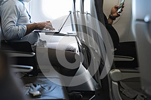 Businessman using laptop in airplane and passenger in front row with cellphone