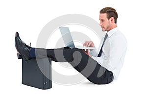 Businessman using laptop with feet up on briefcase