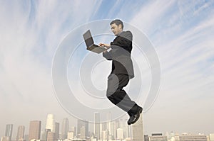 Businessman Using Laptop In Midair With Cityscape In Background