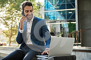 Businessman using a laptop outside and talking on his cellphone photo