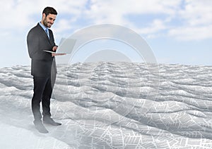 Businessman using laptop in sea of documents under sky clouds