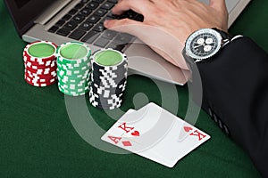 Businessman Using Laptop By Stacked Poker Chips And Cards