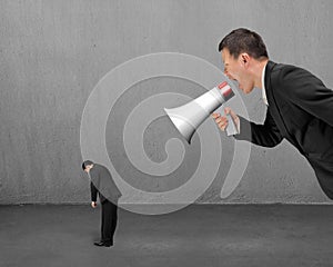 Businessman using megaphone yelling at his employee with concrete room