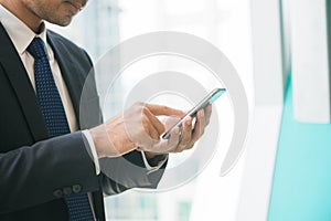 Businessman using mobile phone app texting outside of office in urban city with skyscrapers buildings in the background.