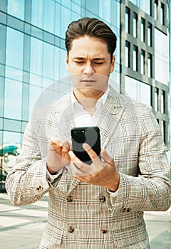 Businessman using mobile phone app texting outside of office in urban city with skyscrapers buildings in the background.