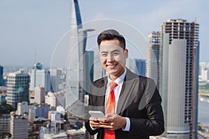 Businessman using mobile phone app texting outside of office in urban city with skyscrapers buildings in the background. Young