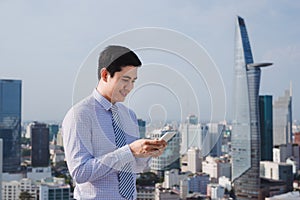 Businessman using mobile phone app texting outside of office in urban city with skyscrapers buildings in the background