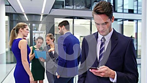 Businessman using mobile phone and colleague discussing in background