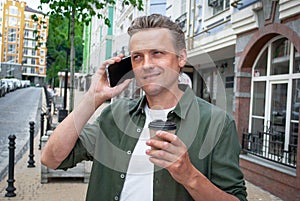 businessman using mobile phone holding coffee craft cup on the street. Handsome Man standing outside a building holding