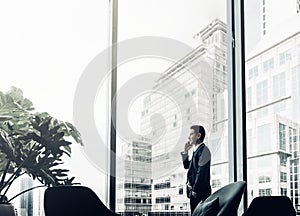 Businessman using mobile phone near office window at corridor ar