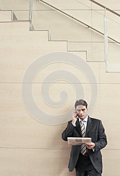 Businessman Using Mobile Phone While Reading Newspaper In Office