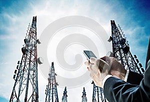 Businessman using mobile phone with Telecommunication towers with TV antennas and satellite dish