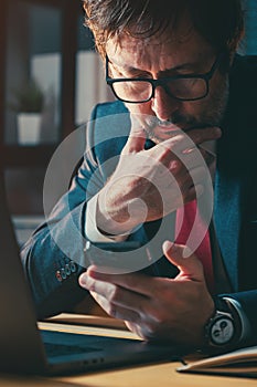 Businessman using mobile phone at work desk in office, checking electronic banking and finance app on smartphone photo
