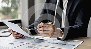 A businessman using a pen to point a pie chart on a document, he is reviewing financial documents from the finance department