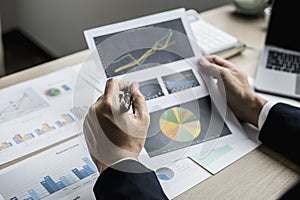 A businessman using a pen to point a pie chart on a document, he is reviewing financial documents from the finance department.