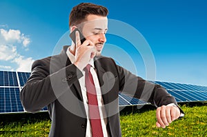 Businessman using phone and checking time on photovoltaic field