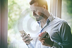 Businessman using smart phone and eating apple