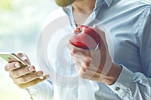 Businessman using smart phone and eating apple