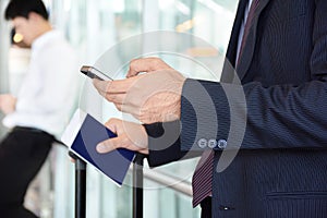 Businessman using smart phone while holding passport in another