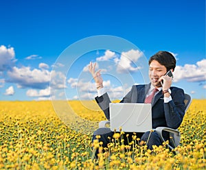 Businessman using smartphone and laptop in flower field