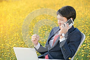 Businessman using smartphone and laptop in flower field