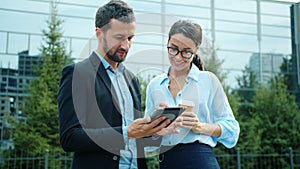 Businessman using tablet outdoors talking to woman holding take out coffee