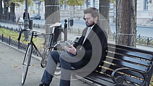Businessman using a tablet sitting on a bench near the bicycle