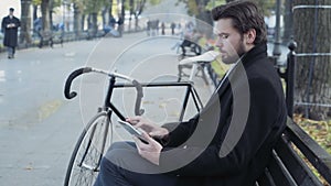 Businessman using a tablet sitting on a bench near the bicycle