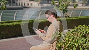 businessman using tablet for work, man sitting on bench on embankment and working online