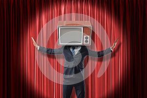Businessman with vintage tv set instead of head raising arms on red stage curtains background