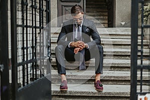 Businessman waiting on the stairs and looking at the time