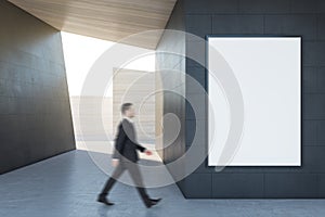 Businessman walking in abstract concrete tile space interior background with empty white mock up poster and sunlght. Design and