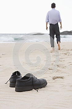 Businessman walking barefoot on beach