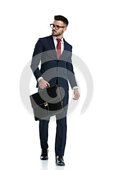 Businessman walking with briefcase on hand and looking away tough