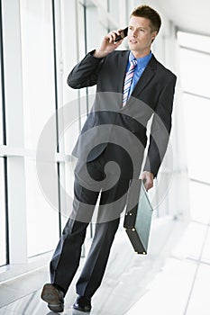 Businessman walking in corridor using mobile phone