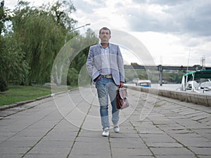 Businessman walking down the street. Mature office worker on the urban background. Male confidence concept. Copy space.