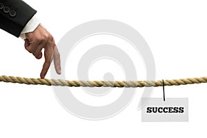 Businessman walking his fingers along a length of rope or a tightrope towards success