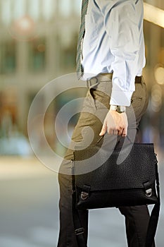 Businessman walking and holding a leather briefcase in his hand. Modern city behind
