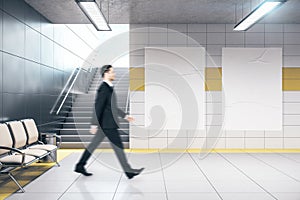 Businessman walking in metro station and two blank banners on wall